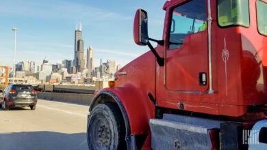 Image of a red truck on a road facing the backdrop of the city of Chicago skyline.