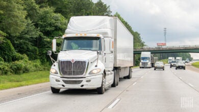 A white sleeper cab pulling a white trailer on a highway