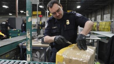 A U.S. Customs and Border Protection officer opens a package on a conveyor belt inside a warehouse to inspect it for counterfeit goods.