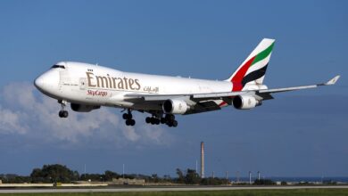 An Emirates SkyCargo jumbo jet with stripped tail approaches a runway.