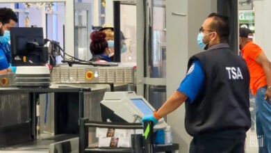 A TSA security agent screens carry-on bags at an airport.