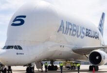 An Airbus Beluga freighter jet, with a bulbous fuselage, sits on the tarmac with workers milling about.