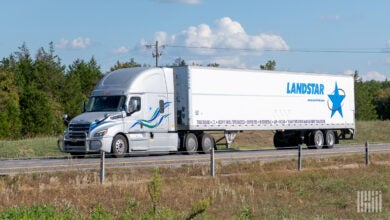 A silver sleeper cab pulling a white Landstar dryvan trailer on a highway