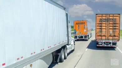 A rearview of an orange Schneider dryvan trailer and an orange Schneider intermodal container being pulled on a highway