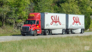 a red Saia daycab pulling two white Saia pup trailers