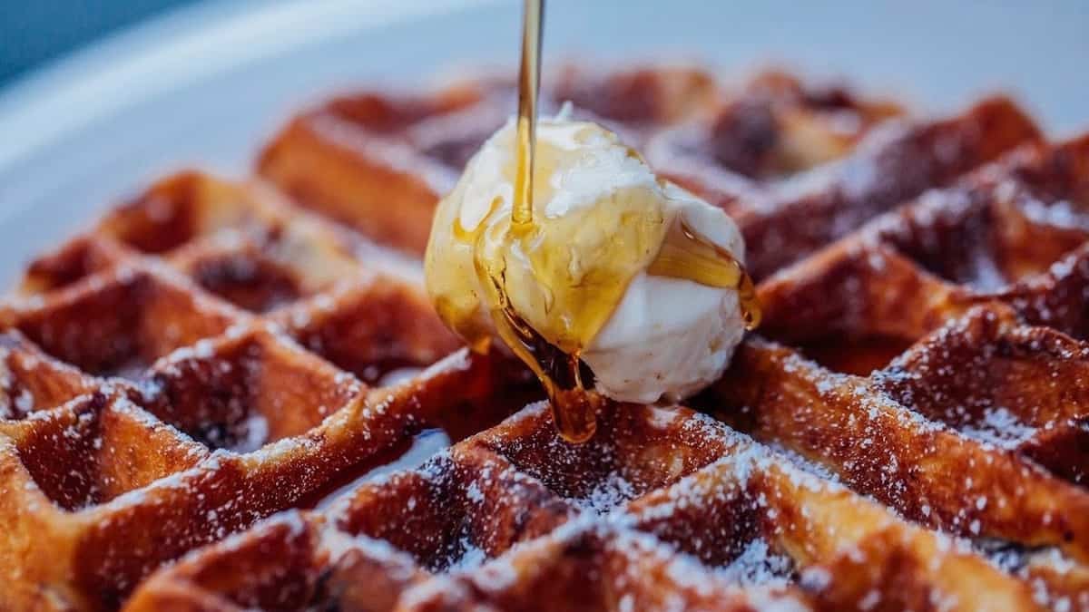 Closeup of maple syrup pouring onto butter and waffle