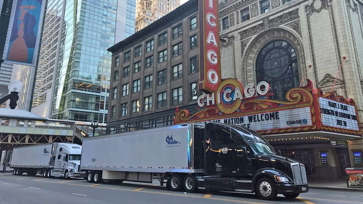 A photograph of two trucks lined up in front of a theater. They are waiting on a city street.