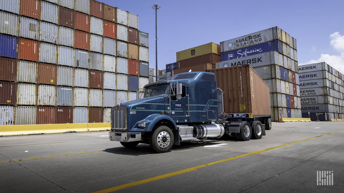 A tractor pulls a flatbed trailer carrying an intermodal container.