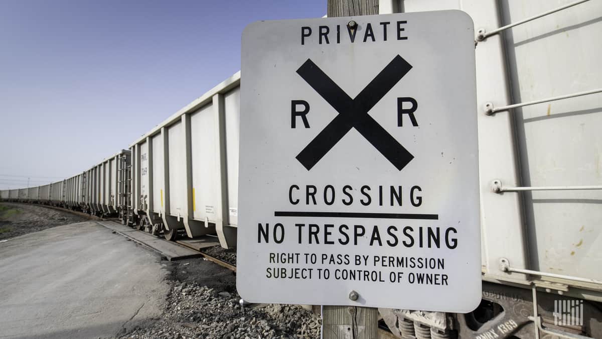 A line of hopper cars stretches into the distance at a private rail crossing.