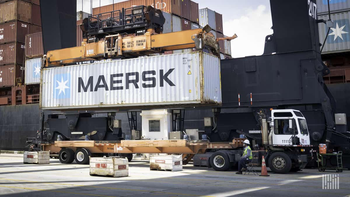 A container comes off a ship and is loaded onto a flatbed trailer.