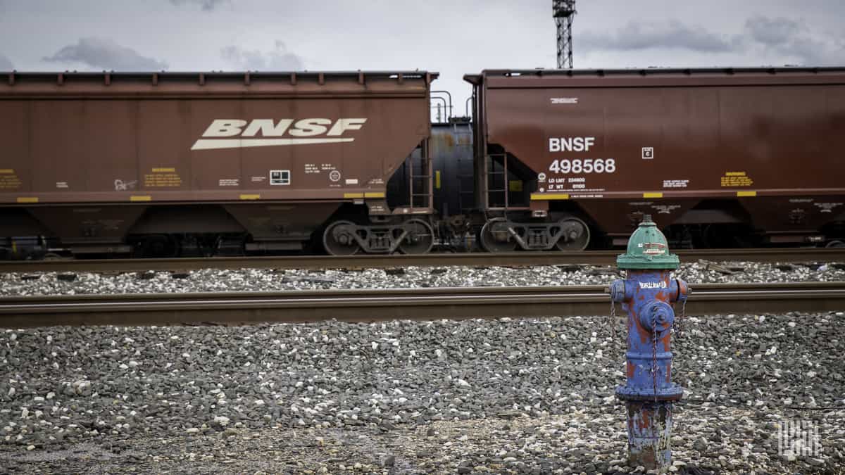 Two BNSF hopper railcars with a tank car on track behind them.