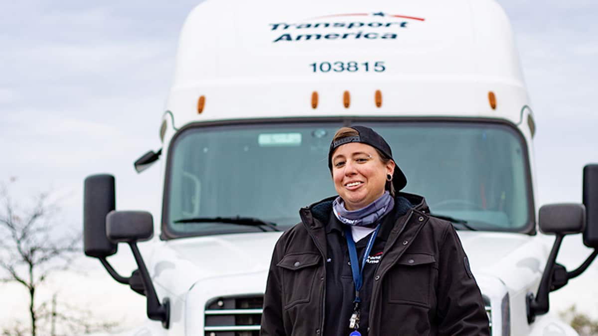 A Transport America driver in front of a tractor-trailer. The carrier has been shifting drivers to dedicated trucking services.