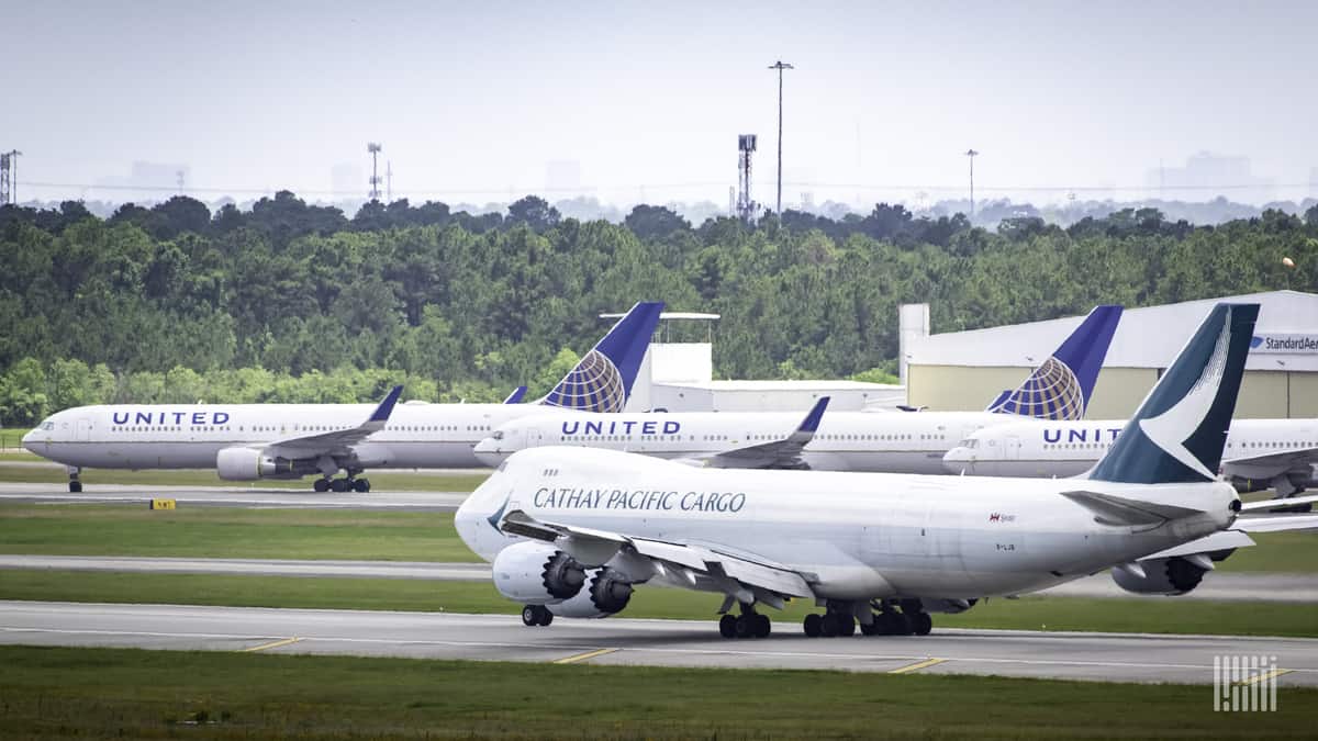 A white jumbo jet begins to move down runway with parked planes in the background.