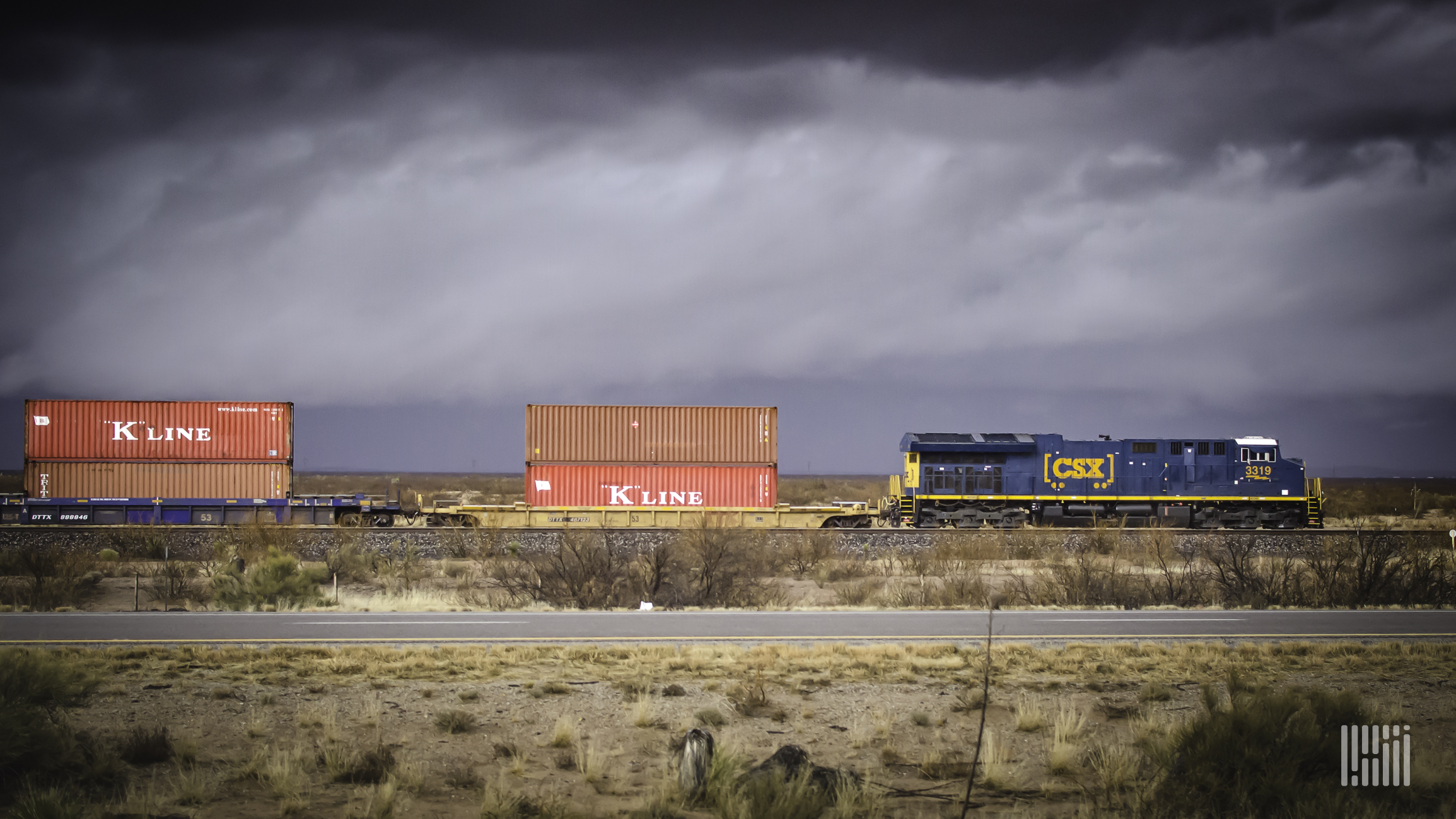 A photograph of a CSX intermodal train rolling through a desert field.