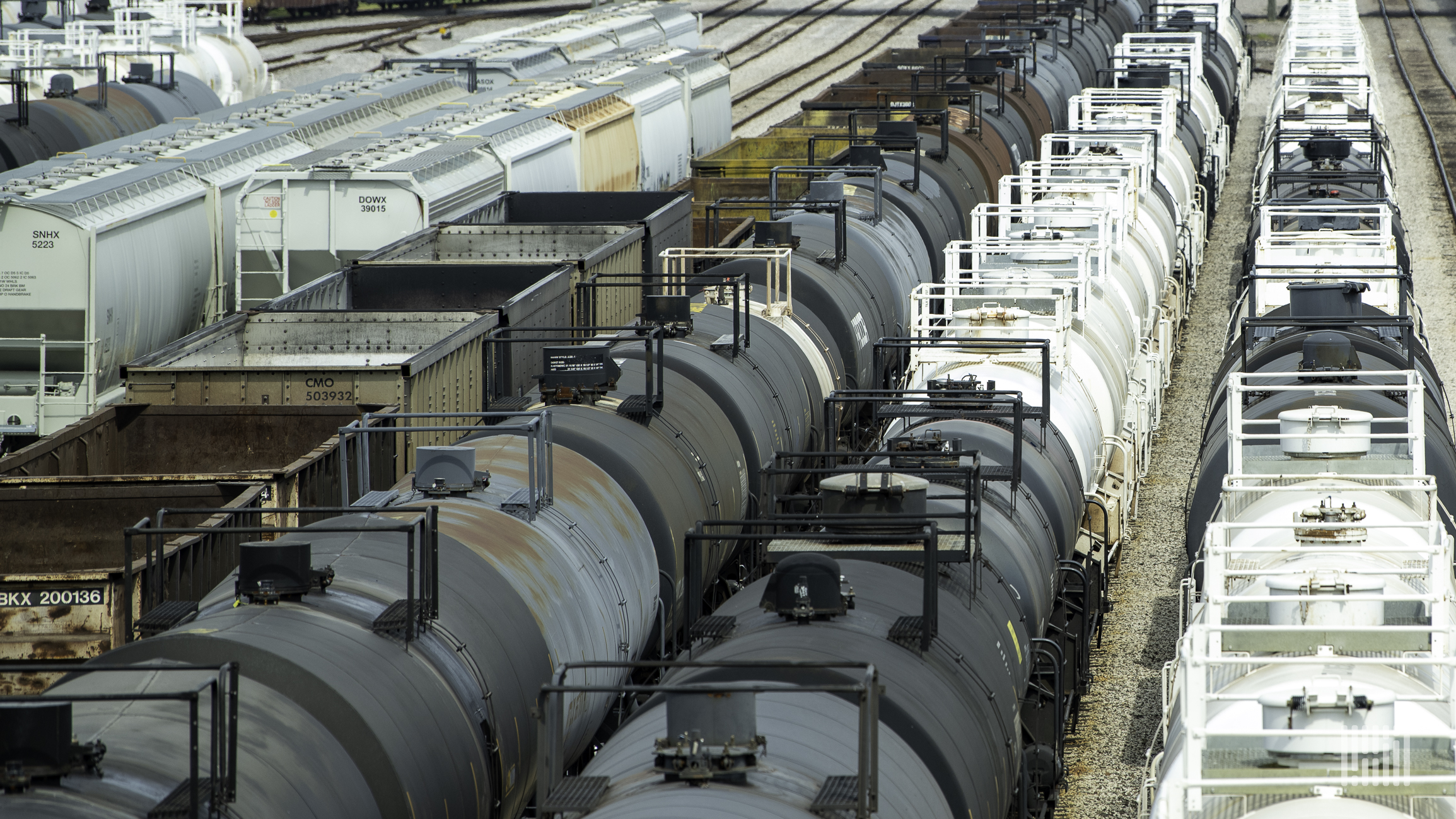 A photograph of a tank cars and grain hoppers parked in a rail yard.