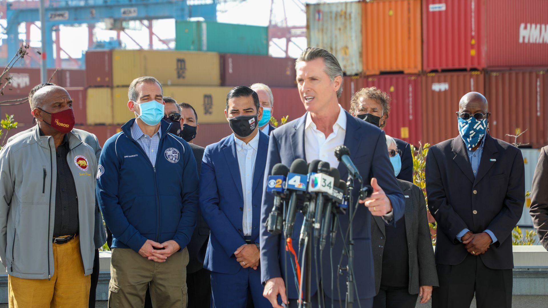 California Gov. Gavin Newsom flanked by officials and longshoremen at the Port of Long Beach during a press conference.