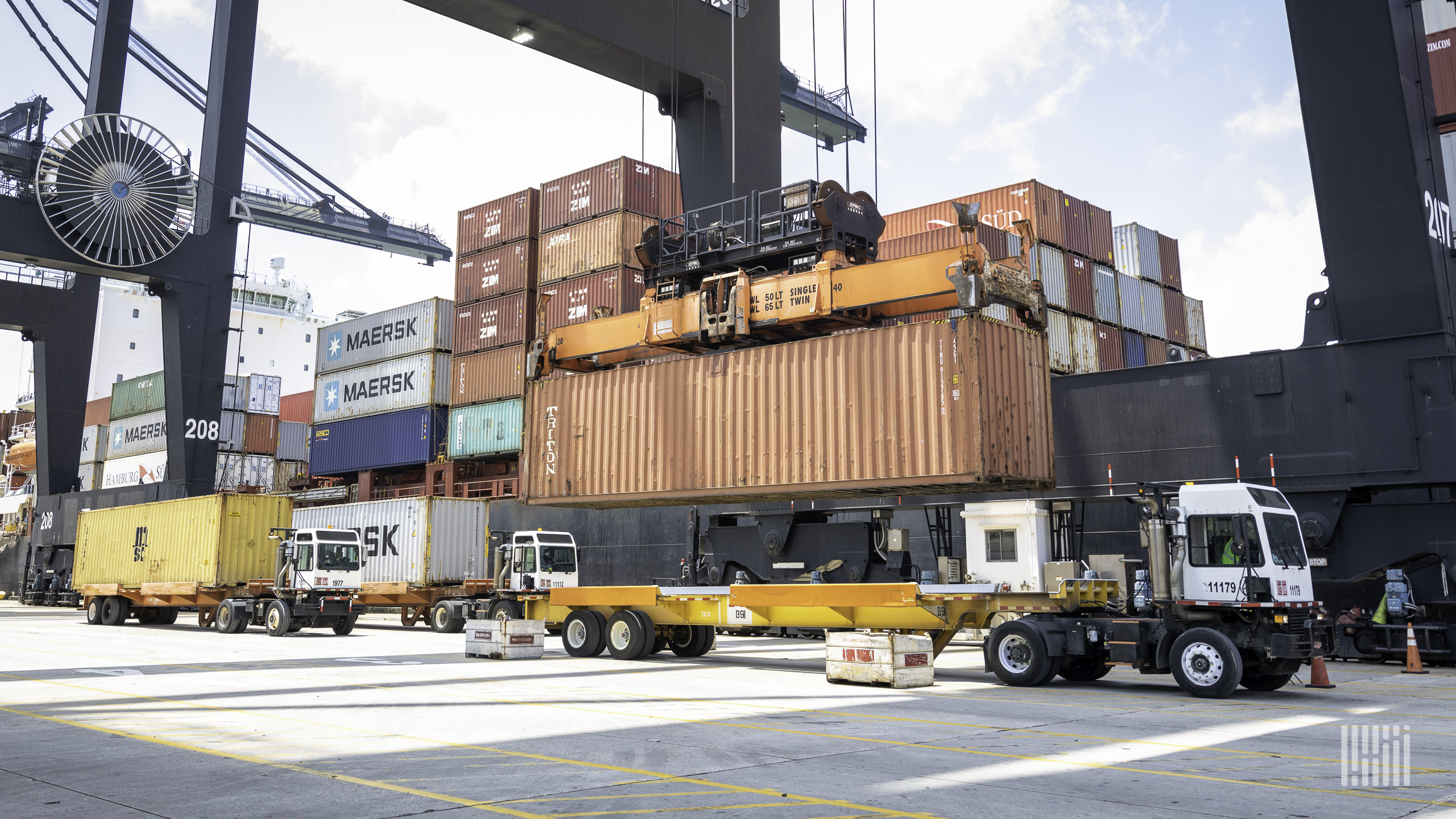 A crane lowers a container from a vessel onto a shuttle cart.