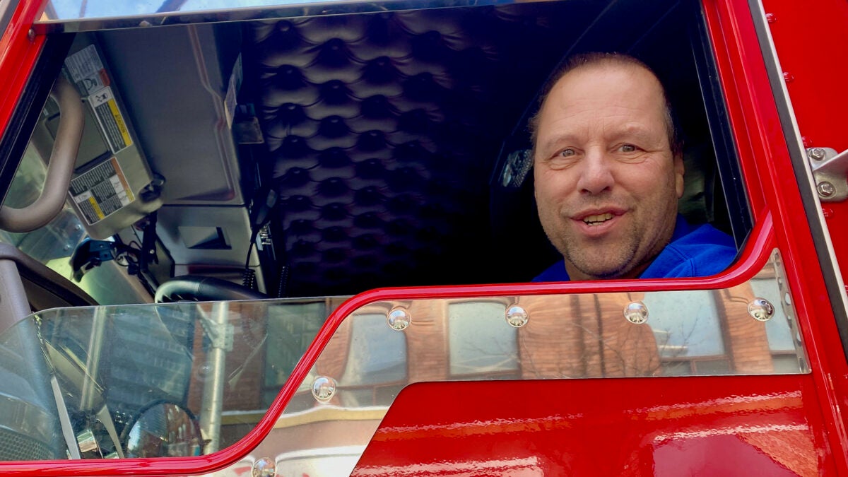 A truck driver smiles through the window of the can of his truck.