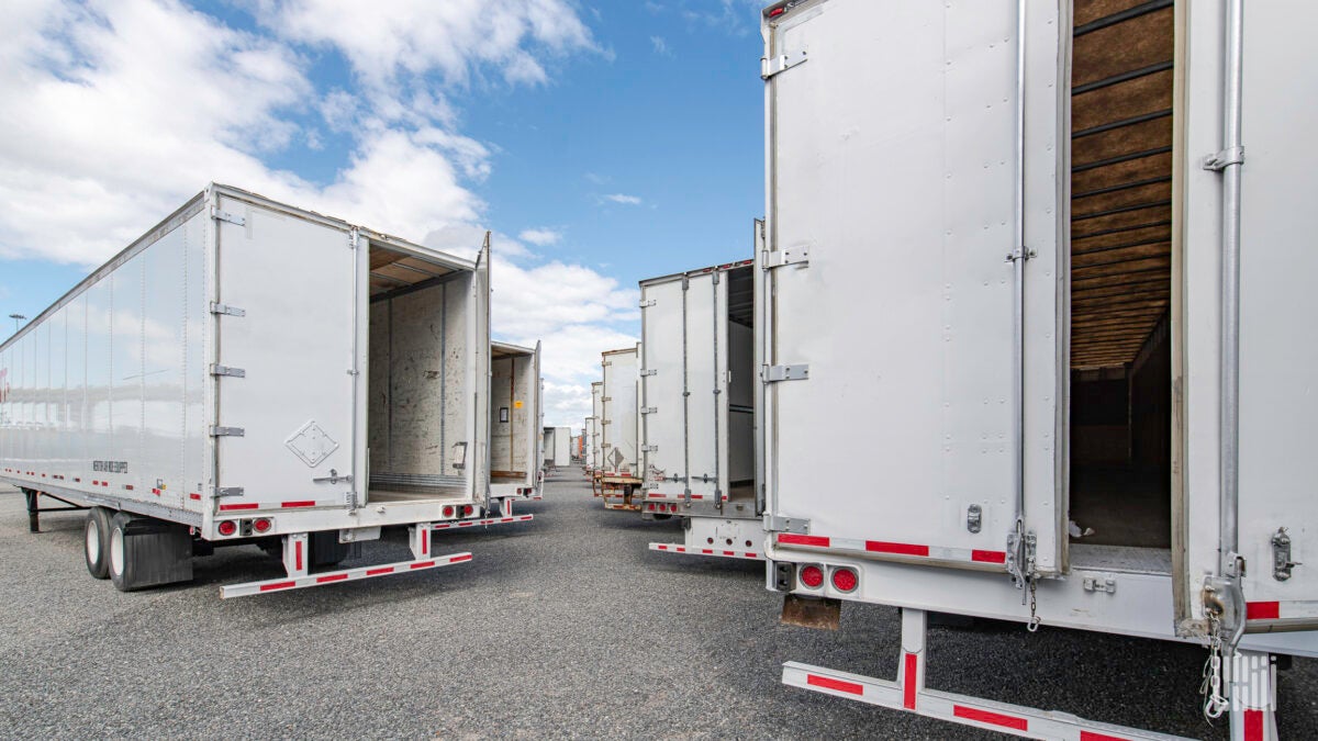 Multiple white commercial trailers are lined up diagonally with their doors open