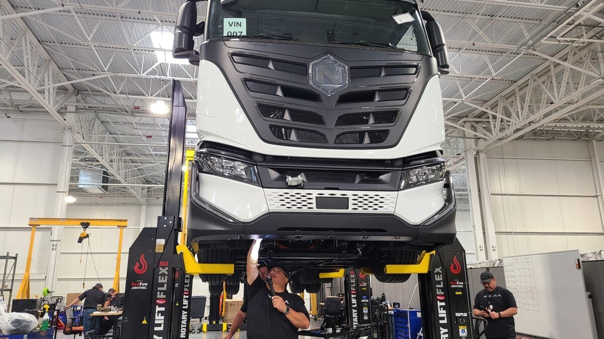 Workers inspect underside of white Nikola Tre Class 8 electric truck.