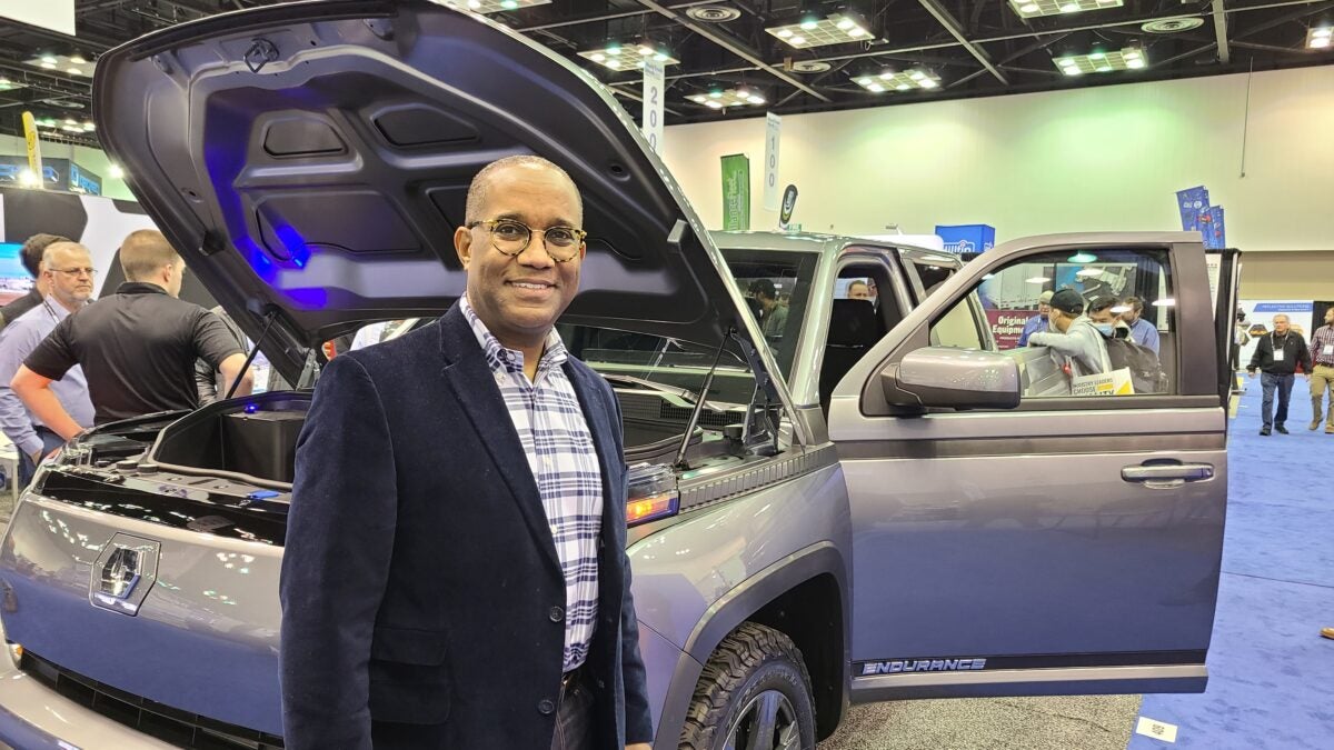 Lordstown Motors President Ed Hightower with silver Endurance electric pickup truck in  background with hood and doors open.