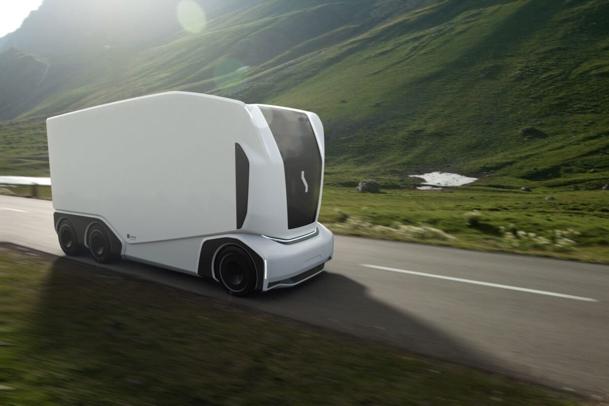 An Einride Pod autonomous vehicle against a backdrop of green hills.