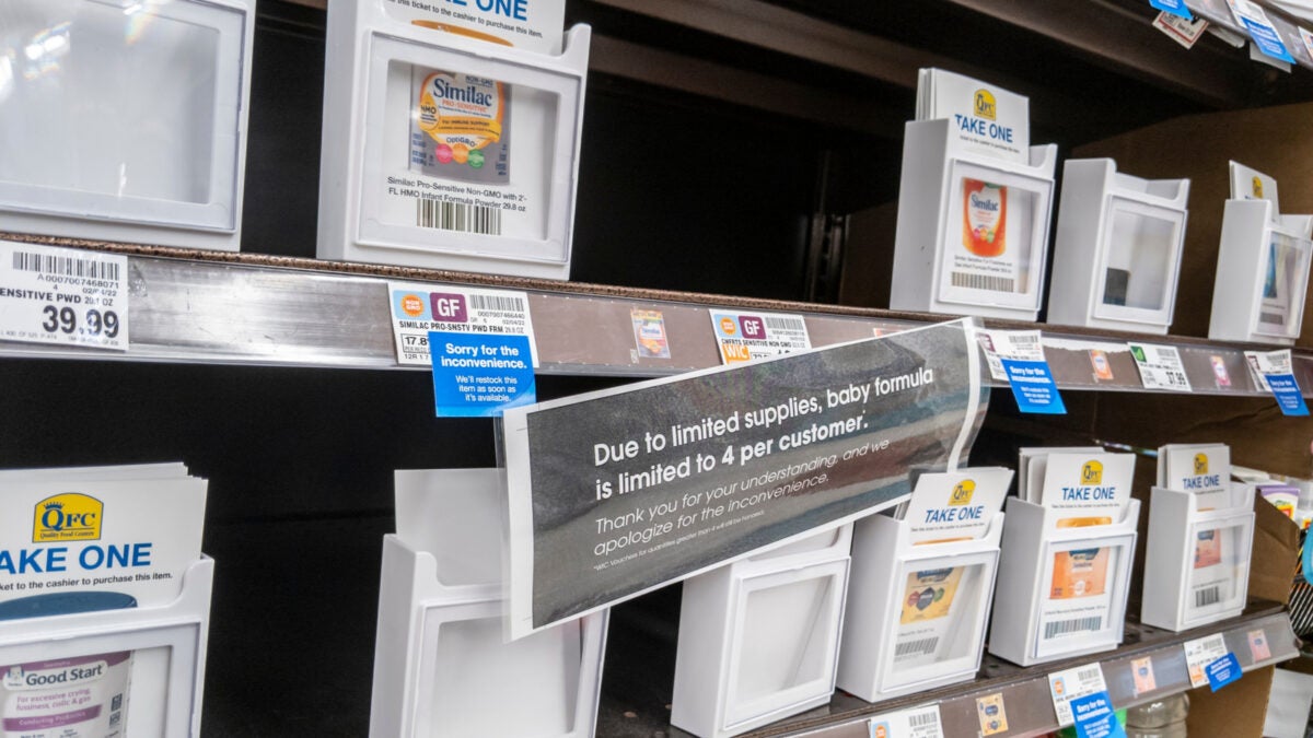 A shelve in a supermarket showing a limited amount of baby formula available, with a sign reading "Due to limited supplies, baby formula is limited to 4 per customer)