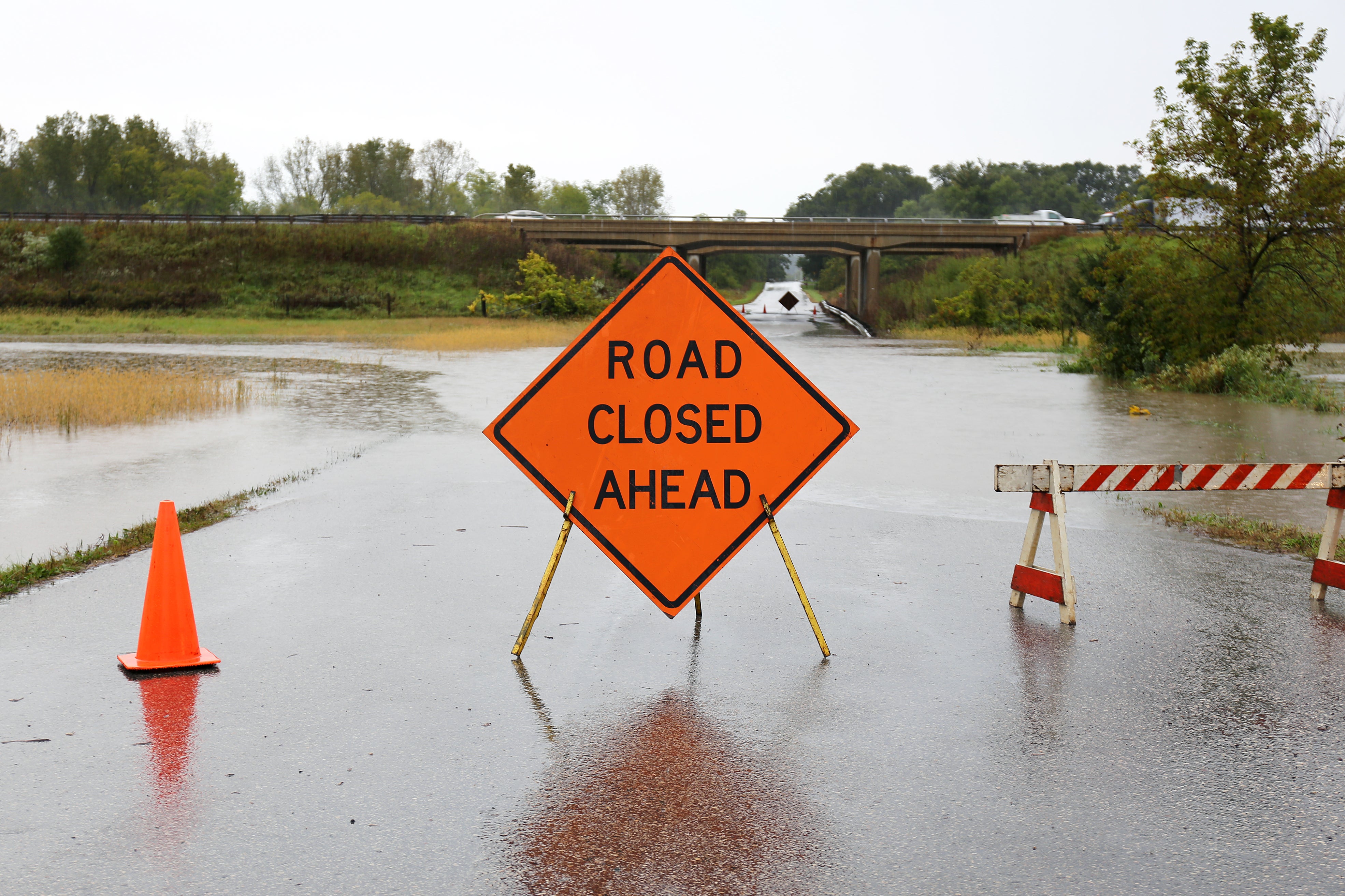 Orange "Road Closed Ahead" sign near flooded highway.