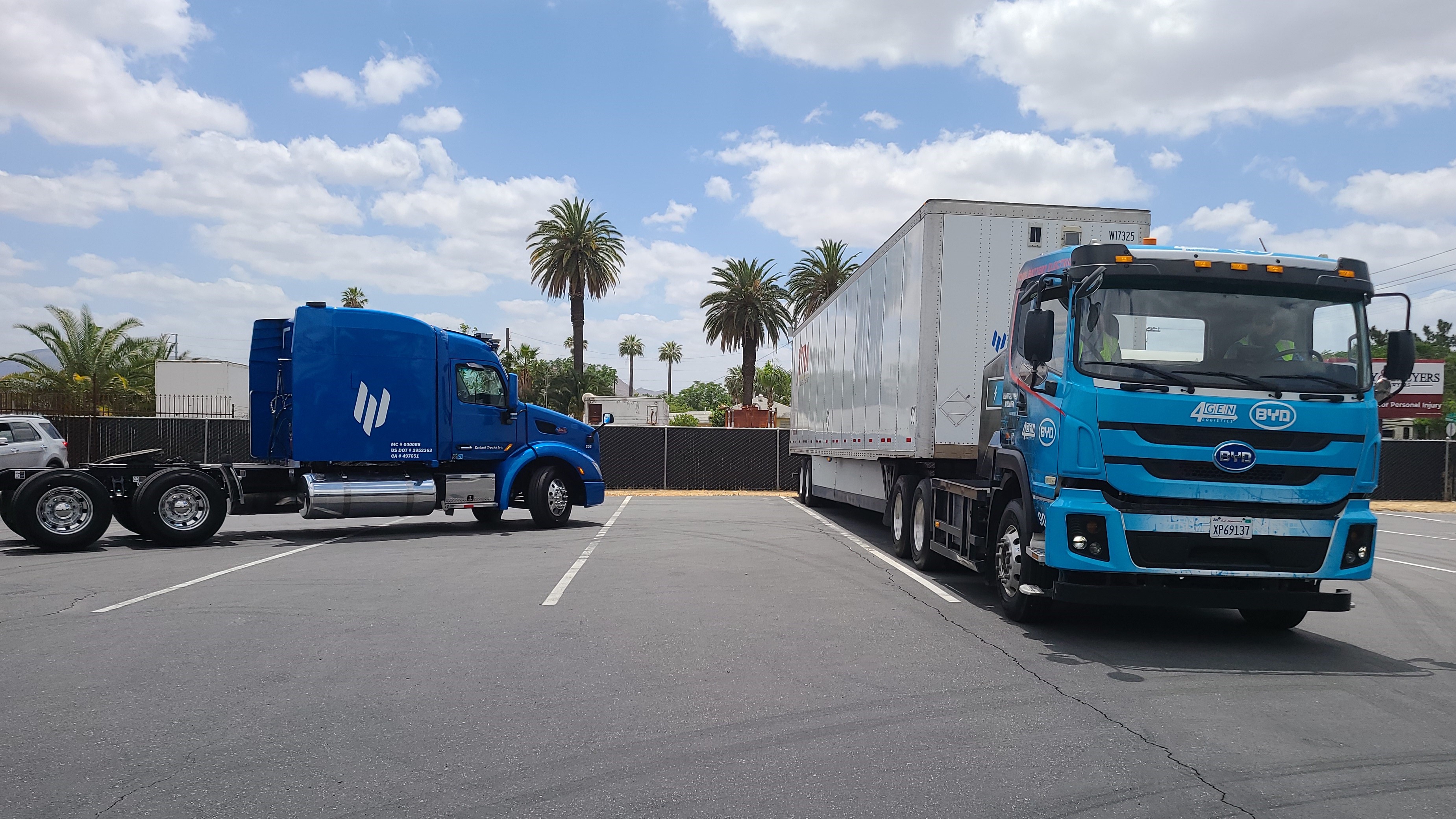 Light blue BYD cabover in foreground. Blue Embark autonous truck in background preparing for a drop and hook of a trailer of HP Inc. computer printers.