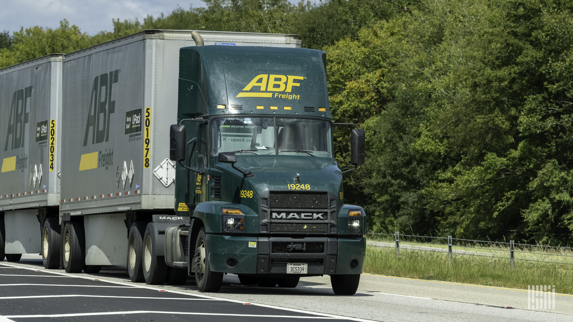 A green ArcBest tractor pulls a silver trailer on a road in front of green trees.