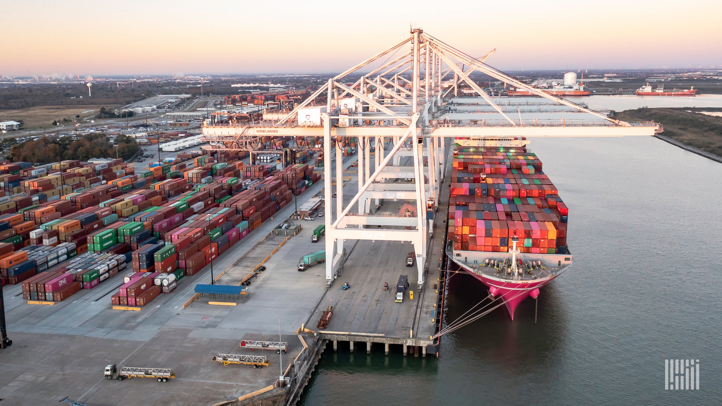 A container ship is docked at port with shipping containers in the background.