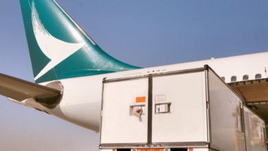 Close up of Cathay Pacificl aircraft's green tail with swoosh logo, with a large container going in side door.