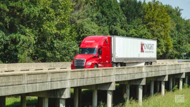 A red Knight tractor pulling a white Knight trailer across a single-lane bridge