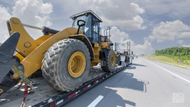 A tractor pulling a flatebed trailer with a wheel loader