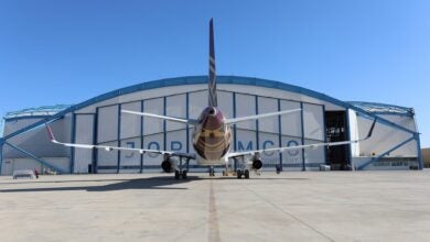 Rear view of a jetliner in front of a hangar with a clear blue sky.