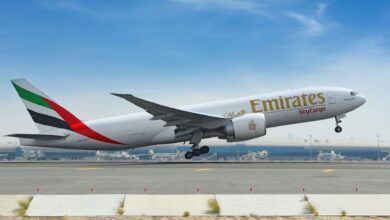 Emirates SkyCargo jet with green, red and black tail lifts off from runway.